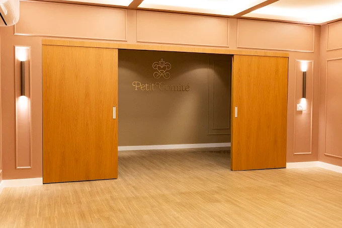 Portas de madeira se abrindo para o salão principal com a logo Petit Comité na parede